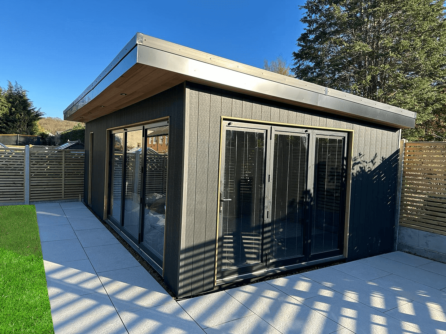 2 x 3 pane aluminium bifold doors in black with black blinds on a garden room
